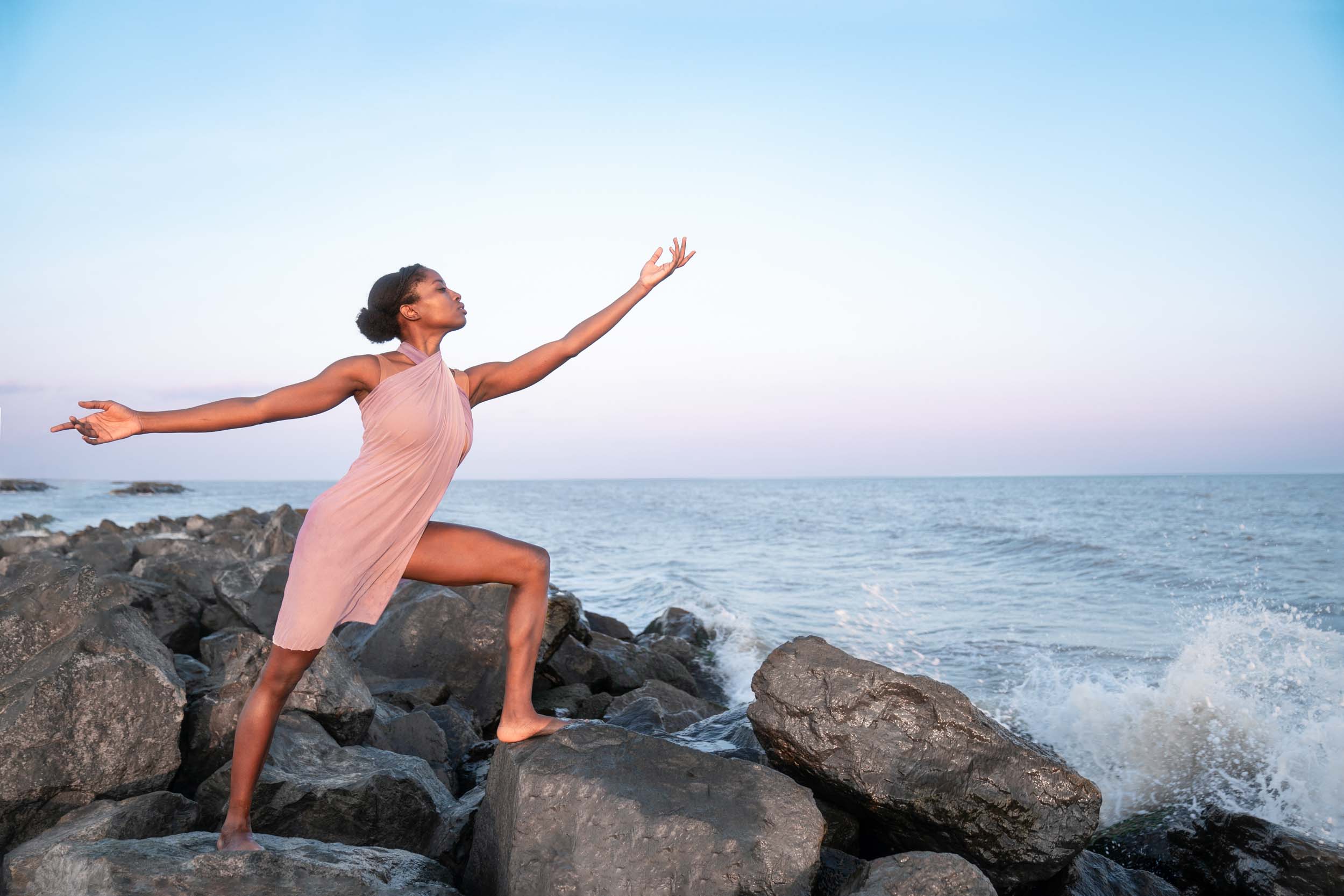 Woman standing on beach rocks and reaching hand to the sky at sunset along the Louisiana Gulf Coast