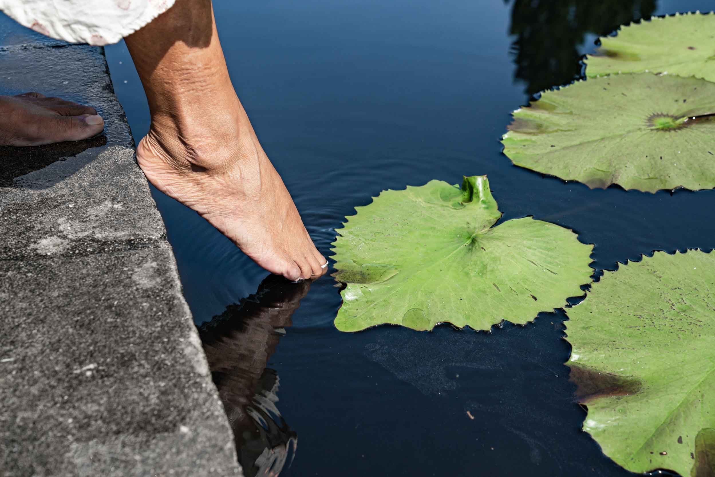 Woman meditating and placing her foot in pond in New Orleans City Park Botanical Garden