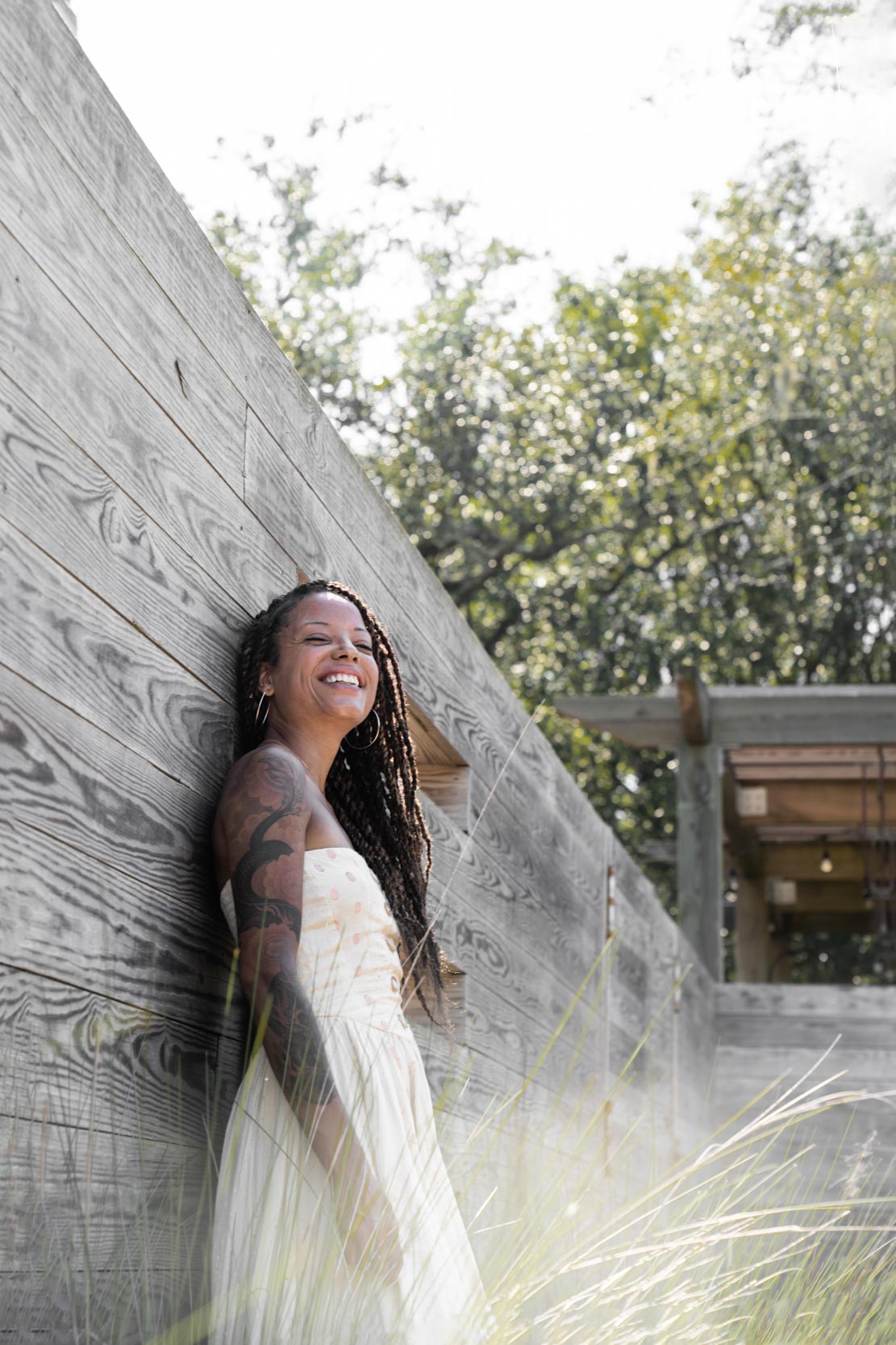 Woman leaning up against wall and laughing on sunny day in City Park Botanical Garden