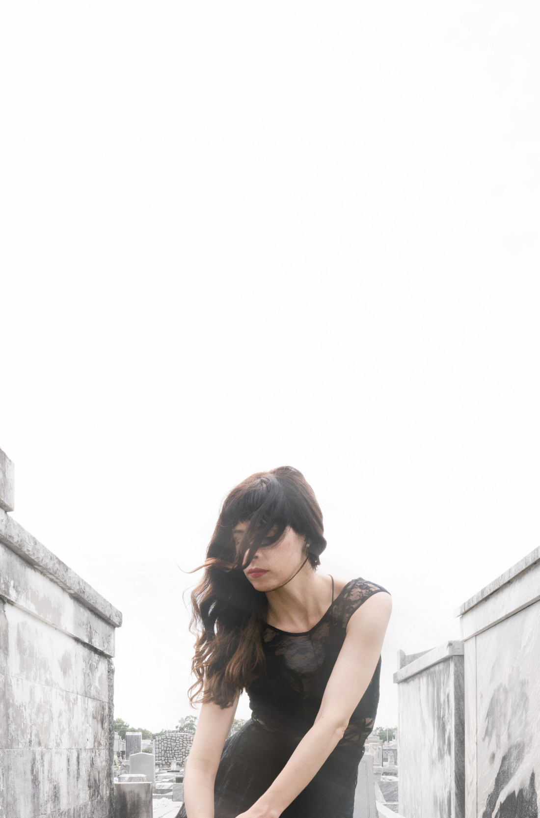 A woman reflecting in a New Orleans cemetery with her hair blowing in the wind